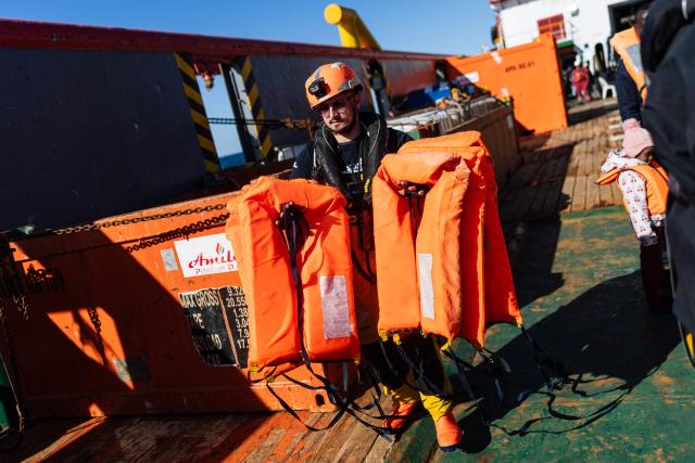 A crew member of the “Ocean Viking” rescue ship distributes life jackets as they prepare to evacuate migrants from the oil tanker the 'Maridive 703' to RHIBs (Rigid inflatable boat), in the search-and-rescue zone of the international waters between Malta and Tunisia, on December 31, 2025. 33 migrants were rescued by crew members of the migrants rescue ship "Ocean Viking" operated by the French NGO SOS Mediterranee. They had been stranded on the oil tanker the 'Maridive 703' since their initial rescue 5 days ago in the joint search zone between Malta and Tunisia in international Mediterranean waters. (Photo by Sameer Al-DOUMY / AFP)