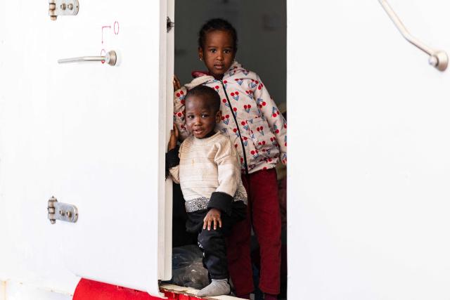 Children stand on the door of the women shelter on the “Ocean Viking” rescue ship after being evacuated by RHIB (Rigid inflatable boat) from the oil tanker the 'Maridive 703' in the search-and-rescue zone of the international waters between Malta and Tunisia, on December 31, 2025. 33 migrants were rescued by crew members of the migrants rescue ship "Ocean Viking" operated by the French NGO SOS Mediterranee. They had been stranded on the oil tanker the 'Maridive 703' since their initial rescue 5 days ago in the joint search zone between Malta and Tunisia in international Mediterranean waters. (Photo by Sameer Al-DOUMY / AFP)