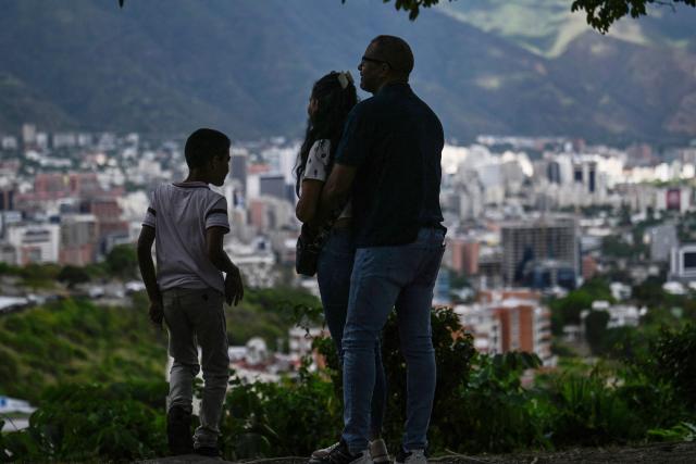 A couple with a kid looks at the city of Caracas on December 31, 2025. The United States announced sanctions on four companies Wednesday over their operations in Venezuela's oil sector, in the latest effort to put pressure on the nation's President Nicolas Maduro. (Photo by Juan BARRETO / AFP)
