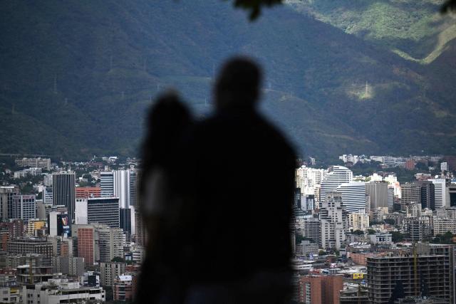 A couple looks at the city of Caracas on December 31, 2025. The United States announced sanctions on four companies Wednesday over their operations in Venezuela's oil sector, in the latest effort to put pressure on the nation's President Nicolas Maduro. (Photo by Juan BARRETO / AFP)