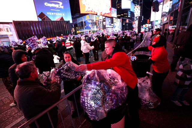 Revelers receive party hats ahead of the 2026 New Year's Eve ball drop in Times Square on December 31, 2025 in New York. (Photo by John Lamparski / AFP)