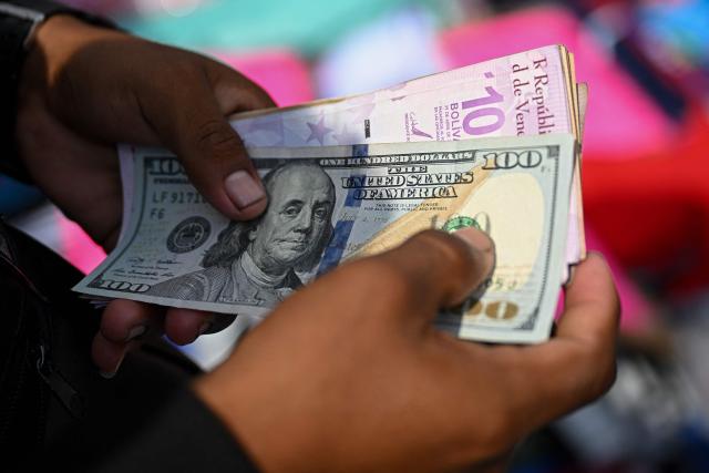 (FILES) A vendor counts Venezuelan bolivar and US dollar banknotes at La Hoyada market in Caracas on December 23, 2025. On December 31, 2025, the Central Bank of Venezuela (BCV) valued the dollar at 301.37 bolivars (Venezuelan currency), a price valid until January 2, representing an increase of 479.25% compared to the 52.02 bolivars set by the issuing entity at the beginning of 2025. (Photo by Federico PARRA / AFP)
