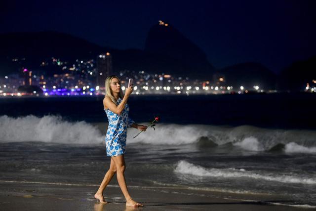 A woman takes pictures with her mobile phone on the eve of New Year's celebrations at Copacabana Beach in Rio de Janeiro, Brazil, on December 31, 2025. (Photo by Daniel RAMALHO / AFP)