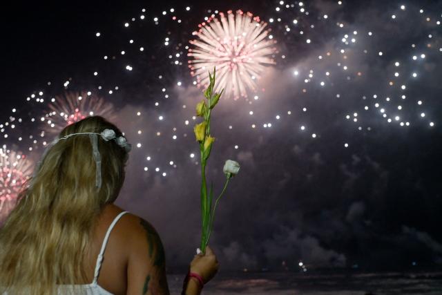 A woman holds a bouquet of flowers as she celebrates during the traditional New Year's fireworks at Copacabana Beach in Rio de Janeiro, Brazil, on January 1, 2026. Rio de Janeiro received, on December 30, 2025, the title of the world’s largest New Year’s Eve celebration from the Guinness World Records, a recognition of its famous massive festivity with live music shows by the sea. (Photo by TERCIO TEIXEIRA / AFP)