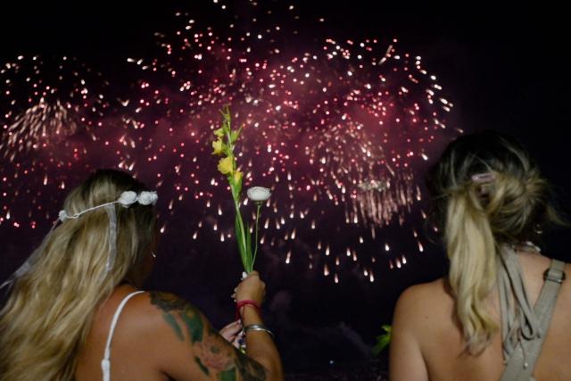 A woman holds a bouquet of flowers as she celebrates during the traditional New Year's fireworks at Copacabana Beach in Rio de Janeiro, Brazil, on January 1, 2026. Rio de Janeiro received, on December 30, 2025, the title of the world’s largest New Year’s Eve celebration from the Guinness World Records, a recognition of its famous massive festivity with live music shows by the sea. (Photo by TERCIO TEIXEIRA / AFP)