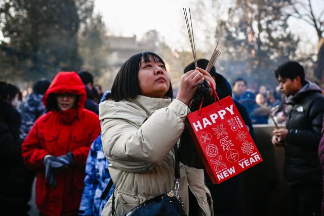 A woman burns incense sticks and offers prayers at Yonghe Temple, also known as Lama Temple, on the first day of the new year in Beijing on January 1, 2026. (Photo by WANG Zhao / AFP)