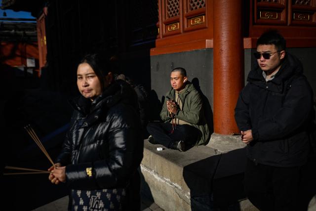 A man (C) offers prayers at Yonghe Temple, also known as Lama Temple, on the first day of the new year in Beijing on January 1, 2026. (Photo by WANG Zhao / AFP)