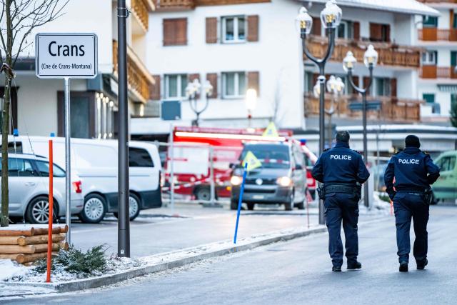 TOPSHOT - Police officers walk near ambulances at the site of an explosion that ripped through a bar in Crans-Montana on January 1, 2026. Several people were killed and others injured when an explosion ripped through a bar in the luxury Alpine ski resort town of Crans Montana, Swiss police said early on January 1. (Photo by MAXIME SCHMID / AFP)