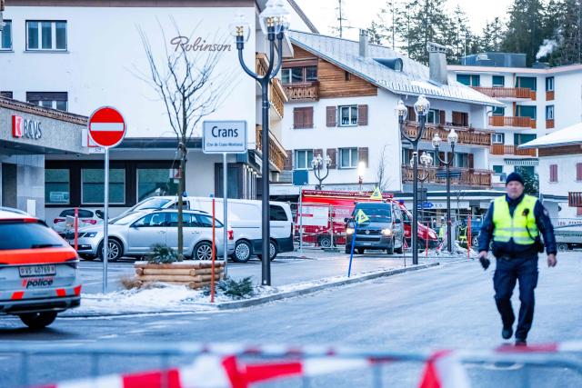 A police officer walks near ambulances at the site of an explosion that ripped through a bar in Crans-Montana on January 1, 2026. Several people were killed and others injured when an explosion ripped through a bar in the luxury Alpine ski resort town of Crans Montana, Swiss police said early on January 1. (Photo by MAXIME SCHMID / AFP)
