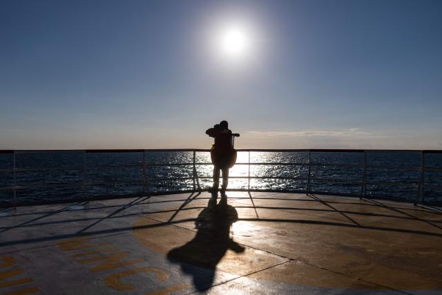 A crew member of the migrants rescue ship "Ocean Viking" operated by the NGO SOS Mediterranee, watch through binoculars as they patrol at the search-and-rescue zone of the international waters between Malta and Tunisia, on December 31, 2025. (Photo by Sameer Al-DOUMY / AFP)