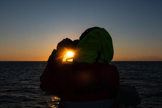 A crew member of the migrants rescue ship "Ocean Viking" operated by the NGO SOS Mediterranee, uses binoculars as they patrol at the search-and-rescue zone of the international waters between Malta and Tunisia, on December 31, 2025. (Photo by Sameer Al-DOUMY / AFP)