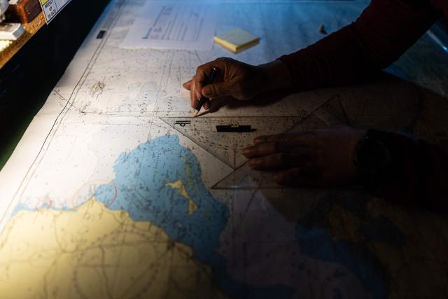 A crew member of the migrants rescue ship "Ocean Viking" operated by the NGO SOS Mediterranee, checks a map as they patrol at the search-and-rescue zone of the international waters between Malta and Tunisia, on December 31, 2025. (Photo by Sameer Al-DOUMY / AFP)