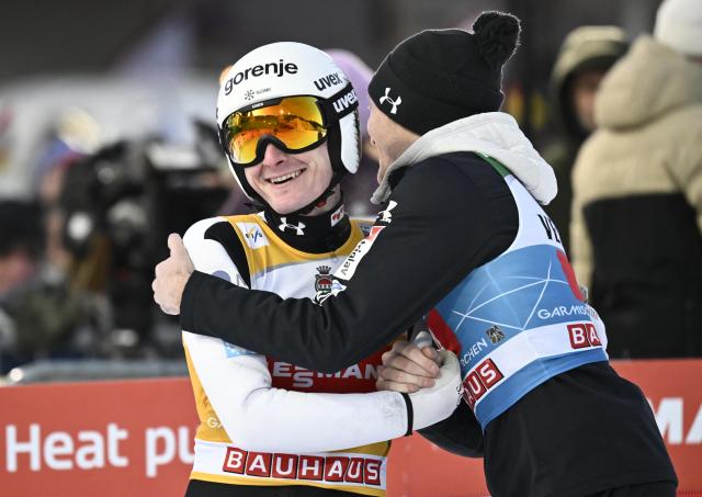 Slovenia's Domen Prevc (L) is congratulated by Slovenia's Anze Lanisek after winning the Men's Individual Large Hill HS142 event of the FIS Ski Jumping World Cup, the second leg of the Four Hills Tournament, in Garmisch-Partenkirchen, southern Germany on January 1, 2026. (Photo by PHILIPP GUELLAND / AFP)