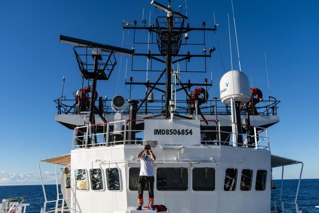 A crew member of the migrants rescue ship "Ocean Viking" operated by the NGO SOS Mediterranee, uses binoculars to watch a Libyan Coast Guard's boat sailing the search-and-rescue zone of the international waters of Malta, on Januray 1, 2026. 33 migrants were rescued by crew members of the migrants rescue ship "Ocean Viking" operated by the NGO SOS Mediterranee. They had been stranded on the oil tanker the 'Maridive 703' since their initial rescue 5 days ago in the joint search zone between Malta and Tunisia in international Mediterranean waters. (Photo by Sameer Al-DOUMY / AFP)