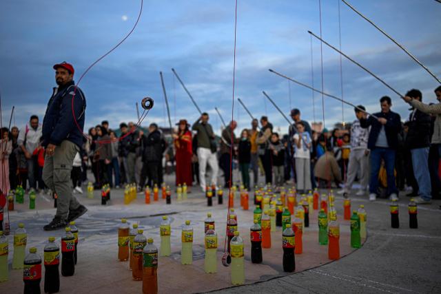 Visitors try to land a ring around the necks of soft drink bottles to catch one during a street vendor’s performance in Marrakesh's Jemaa el-Fna Square on January 1, 2026, during the Africa Cup of Nations (CAN) football tournament. (Photo by Khaled DESOUKI / AFP)