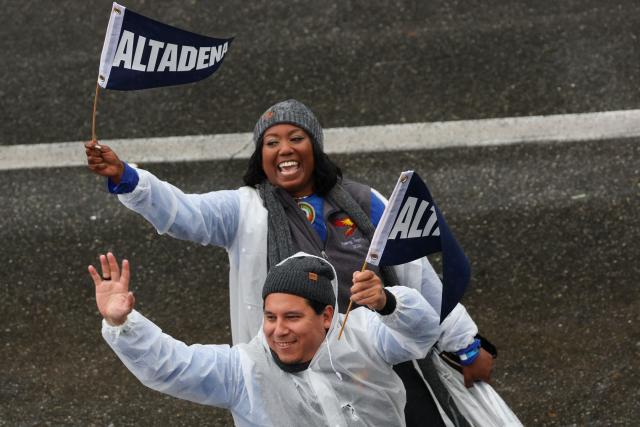 People wave Altadena pennants as they walk alongside The California Community Foundation and Black Freedom Fund “The Rising Together” float to honor victims of the Altadena, Pasadena, Pacific Palisades and Malibu wildfires on  the parade route in the rain during the 137th Rose Parade on New Years Day in Pasadena, California, on January 1, 2026. The parade features floral floats, marching bands and equestrian units to ring in the New Year along the 5.5 mile (8.8 km) route along Colorado Blvd in Pasadena. (Photo by Patrick T. Fallon / AFP)