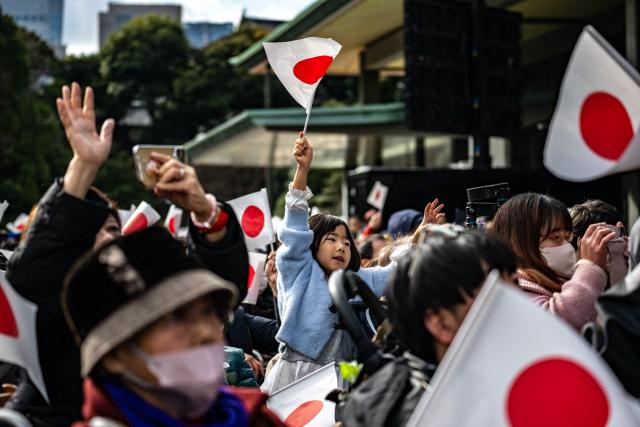 People wave national flags during the traditional New Year's greeting ceremony by Japan's royal family at the Imperial Palace in Tokyo on January 2, 2026. (Photo by Philip FONG / AFP)