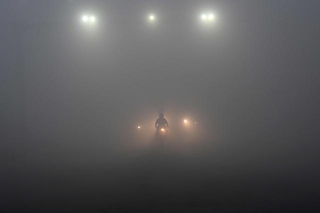 Commuters move along a road engulfed in dense fog on a cold winter morning in Lahore on January 2, 2026. (Photo by Arif ALI / AFP)