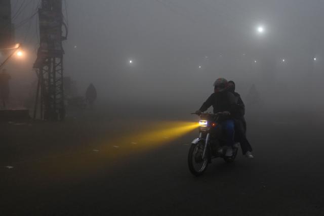 Commuters move along a road engulfed in dense fog on a cold winter morning in Lahore on January 2, 2026. (Photo by Arif ALI / AFP)