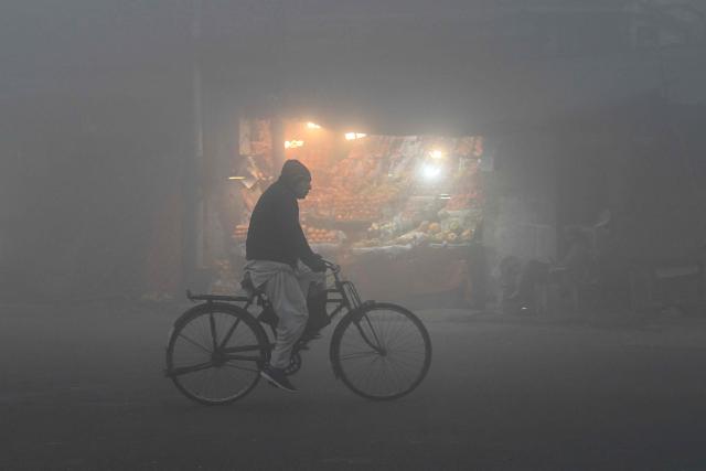 A cyclist moves along a street engulfed in dense fog in Lahore on January 2, 2026. (Photo by Arif ALI / AFP)