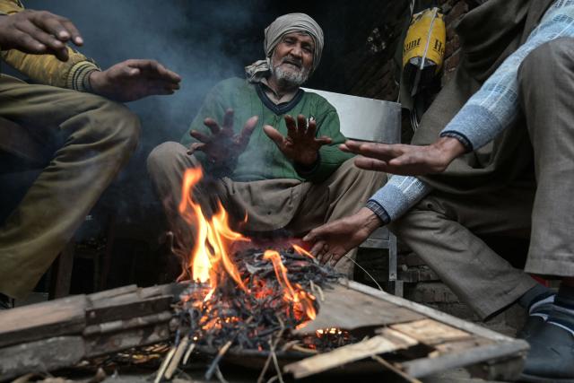 People sit around a bonfire to warm themselves on a cold winter's day in Amritsar on January 2, 2026. (Photo by Narinder NANU / AFP)