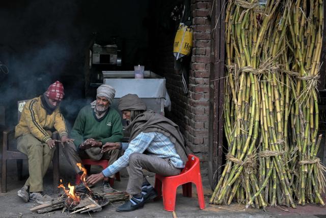 People sit around a bonfire to warm themselves on a cold winter's day in Amritsar on January 2, 2026. (Photo by Narinder NANU / AFP)