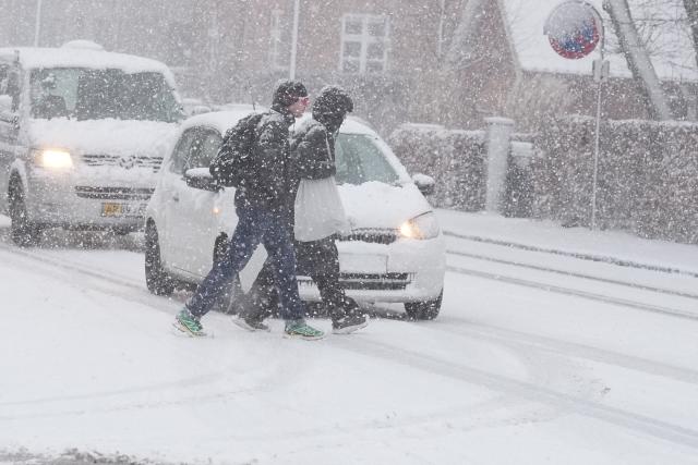 Pedestrians cross a snow-covered street in Aalborg, Denmark, on January 2, 2026, as the country experiences a weather change due to a large low-pressure system. (Photo by Henning Bagger / Ritzau Scanpix / AFP) / Denmark OUT