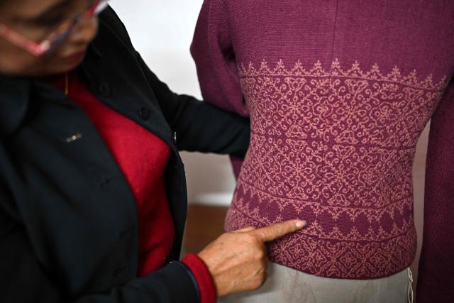 Mexican seamstress and designer Olivia Trujillo Cortes, 63, displays one of the garments made for Mexico's President Claudia Sheinbaum during an interview in her workshop in San Pedro Martir, on the outskirts of Mexico City, on December 23, 2025. Mexican President Claudia Sheinbaum wore a purple, indigenous-embroidered dress at her first meeting with Donald Trump during the 2026 World Cup draw, a choice seen as symbolizing women's power. That week, The New York Times named her among the world's most stylish figures, highlighting her strategy of blending indigenous craftsmanship with modern elegance to send a political message. (Photo by Yuri CORTEZ / AFP)