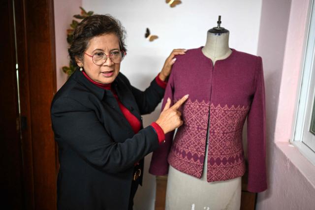 Mexican seamstress and designer Olivia Trujillo Cortes, 63, displays one of the garments made for Mexico's President Claudia Sheinbaum during an interview in her workshop in San Pedro Martir, on the outskirts of Mexico City, on December 23, 2025. Mexican President Claudia Sheinbaum wore a purple, indigenous-embroidered dress at her first meeting with Donald Trump during the 2026 World Cup draw, a choice seen as symbolizing women's power. That week, The New York Times named her among the world's most stylish figures, highlighting her strategy of blending indigenous craftsmanship with modern elegance to send a political message. (Photo by Yuri CORTEZ / AFP)