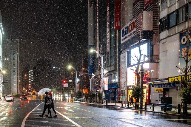 Pedestrians walk with umbrellas as it snows and rains in Tokyo's Akihabara district on January 2, 2026. (Photo by Philip FONG / AFP)