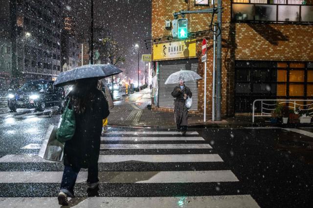 Pedestrians walk with umbrellas as it snows and rains in Tokyo's Koto district on January 2, 2026. (Photo by Philip FONG / AFP)