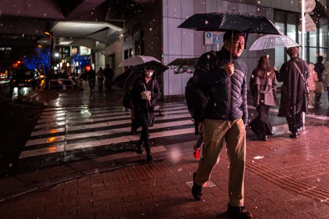 Pedestrians walk with umbrellas as it snows and rains in Tokyo's Akihabara district on January 2, 2026. (Photo by Philip FONG / AFP)