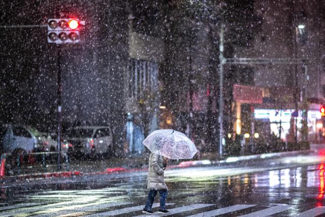 A pedestrian walks with an umbrella as it snows and rains in Tokyo's Koto district on January 2, 2026. (Photo by Philip FONG / AFP)