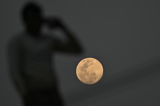 A man speaks on a mobile phone atop a building as the Wolf Moon rises across the sky in Bengaluru on January 2, 2026. (Photo by Idrees MOHAMMED / AFP)