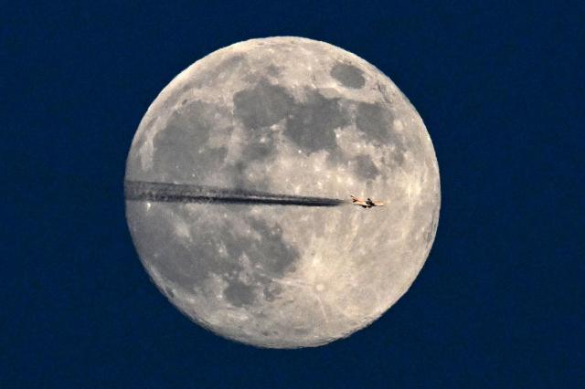 A jet flies past the January full moon, also known as "Wolf Moon", over Frankfurt am Main, western Germany on January 2, 2026. (Photo by Kirill KUDRYAVTSEV / AFP)