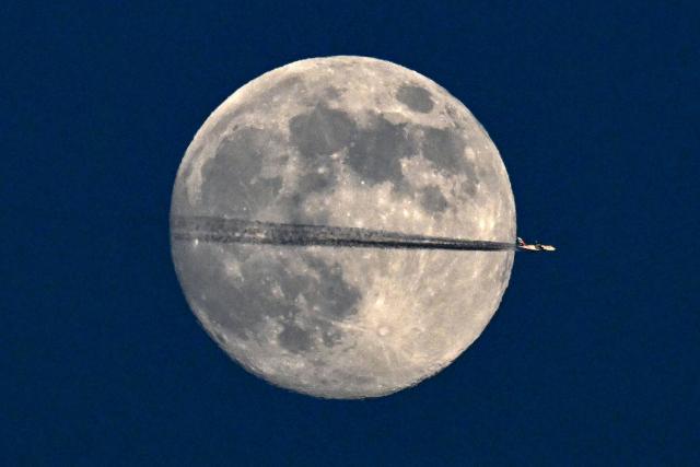 A jet flies past the January full moon, also known as "Wolf Moon", over Frankfurt am Main, western Germany on January 2, 2026. (Photo by Kirill KUDRYAVTSEV / AFP)