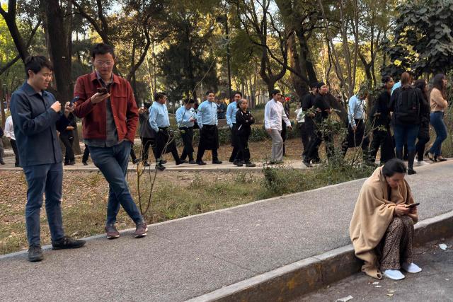 Hotel staff and guests use their mobile phones on the street after evacuating the hotel during a 6.5 magnitude earthquake in Mexico City, on January 2, 2026. A 6.5-magnitude earthquake shook Mexico City and parts of southwestern Guerrero state on Friday, the national seismological service confirmed. (Photo by David GANNON / AFP)