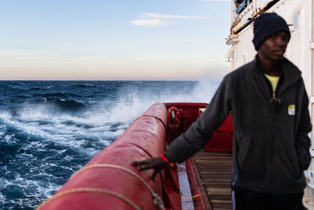 A migrant stands on the deck of rescue ship "Ocean Viking" operated by the NGO SOS Mediterranee as waves crash against the ship sailing in the Mediterranean Sea, near Italy, on January 2, 2026. 33 migrants were rescued by crew members of the migrants rescue ship "Ocean Viking" operated by the NGO SOS Mediterranee. They had been stranded on the oil tanker the 'Maridive 703' since their initial rescue 5 days ago in the joint search zone between Malta and Tunisia in international Mediterranean waters. (Photo by Sameer Al-DOUMY / AFP)