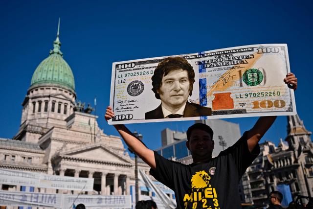 (FILES) A supporter of Argentina's President-elect Javier Milei displays a one hundred dollar bill placard with an image of the future president as he waits outside the Congress before his inauguration ceremony, in Buenos Aires on December 10, 2023. Argentine President Javier Milei enacted the so-called “Fiscal Presumption of Innocence Law,” which raises the minimum thresholds for accusing citizens of tax evasion, with the aim of encouraging the legalization of savings in a context of scarce reserves and imminent debt maturities. (Photo by Luis ROBAYO / AFP)