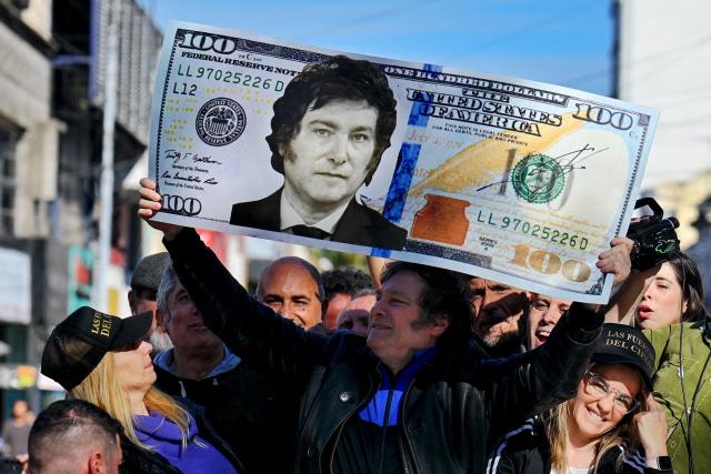 (FILES) Argentine congressman and presidential candidate for the La Libertad Avanza Alliance, Javier Milei (C), holds a giant 100-dollar bill with his face painted on it during a campaign rally in San Martin, Buenos Aires province, Argentina, on September 25, 2023. Argentine President Javier Milei enacted the so-called “Fiscal Presumption of Innocence Law,” which raises the minimum thresholds for accusing citizens of tax evasion, with the aim of encouraging the legalization of savings in a context of scarce reserves and imminent debt maturities. (Photo by Luis ROBAYO / AFP)