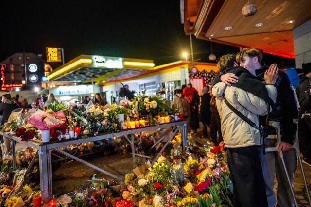 An injured survivor (R) greets a person next to a makeshift memorial near the site of a fire that ripped through a bar during New Year's Eve celebrations in the Alpine ski resort town of Crans-Montana killing around 40 people and injuring more than 100 others, in Crans-Montana on January 2, 2026. Investigators raced on January 2, 2026 to identify the victims of a fire that ripped through a bar in the Swiss Alps town of Crans-Montana, turning a New Year's celebration into one of the country's worst tragedies. Frederic Gisler, police commander in the Wallis canton in southwestern Switzerland, told reporters that authorities had counted "around 40 people who have died and around 115 injured, most of them seriously". (Photo by MAXIME SCHMID / AFP)