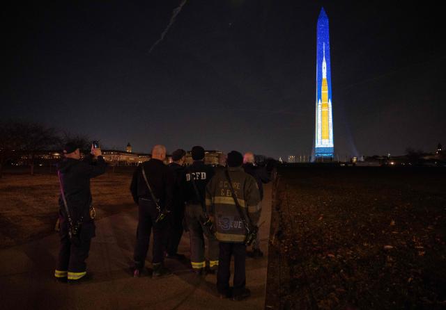 Members of the DC Fire Department take photos of a Saturn V rocket projected onto the Washington Monument during the "Illumination of America" event marking America’s 250th anniversary at the National Mall in Washington, DC, on January 2, 2026. (Photo by ANDREW CABALLERO-REYNOLDS / AFP)