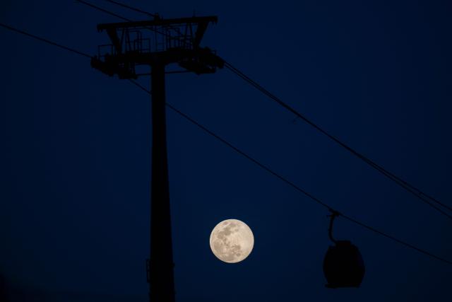 The first moon of the year, the "Wolf Moon," is seen rising next to a cable car in the San Agustin neighborhood in eastern Caracas on January 2, 2026. (Photo by Federico PARRA / AFP)