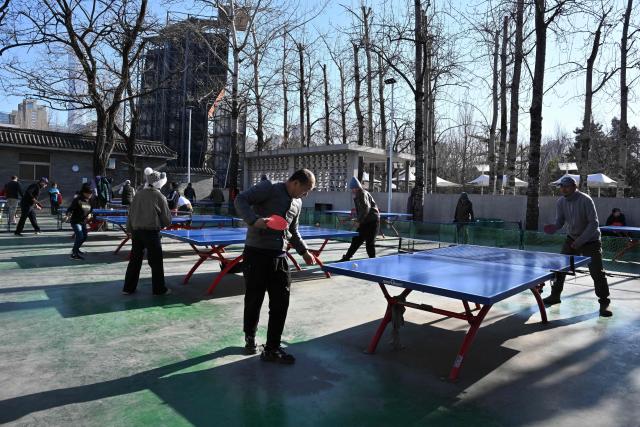 People play table tennis at a park in Beijing on January 3, 2026. (Photo by ADEK BERRY / AFP)