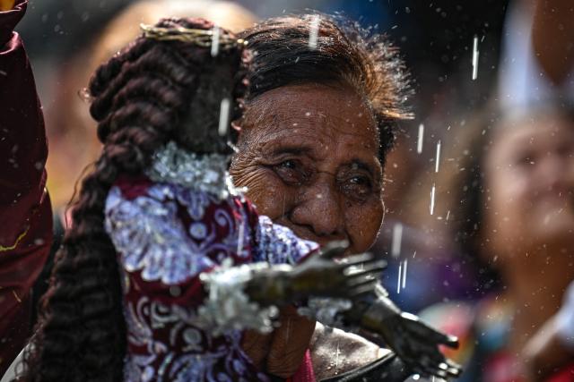 A Catholic devotee reacts as they are showered with holy water during the blessing of Jesus the Nazarene replicas at Quiapo in Manila on January 3, 2026, ahead of the annual "Black Nazarene" procession on January 9 that millions of Catholic devotees are expected to attend. (Photo by Jam STA ROSA / AFP)