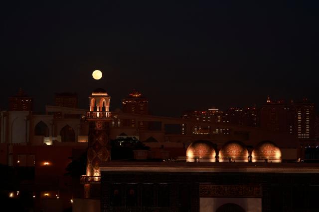 The first supermoon of the year, the ‘Wolf Moon,’ is seen rising behind the Katara Mosque, also known as "Qatar's Turquoise Mosque, in Katara Cultural Village on January 3, 2026. (Photo by Karim JAAFAR / AFP)