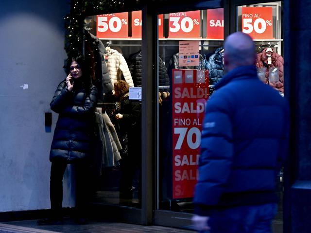 A woman speaks on her mobile phone next to a shopping window advertsing seasonal sales in downtown Rome on January 3, 2026. (Photo by Filippo MONTEFORTE / AFP)