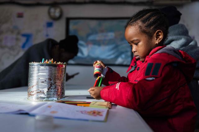 A child colors drawings onboard of the rescue ship "Ocean Viking" operated by the NGO SOS Mediterranee, as they sail at sea to the designated port of disembarkation in Savona, northwestern Italy, on January 3, 2026. 33 migrants were rescued by crew members of the migrants rescue ship "Ocean Viking" operated by the NGO SOS Mediterranee. They had been stranded on the oil tanker the 'Maridive 703' since their initial rescue 5 days ago in the joint search zone between Malta and Tunisia in international Mediterranean waters. (Photo by Sameer Al-DOUMY / AFP)