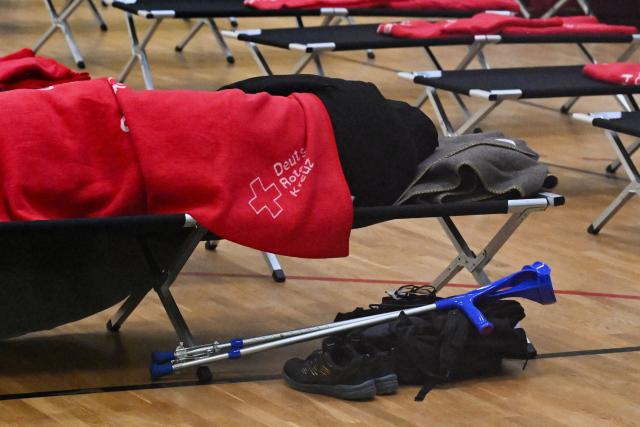 A man sleeps at a heated emergency shelter of the German Red Cross (Deutsches Rotes Kreuz) set up at the Cole Sports Center in southwest Berlin on early January 4, 2026, after power cables in the area were seriously damaged causing a power outage which left tens of thousands of households in the German capital without electricity. The widespread power outage in southwest Berlin, affecting tens of thousands of households, was deliberately caused with incendiary devices, according to Berlin's Senator for Economic Affairs. It was "clearly" a "deliberate act," Senator Giffey said on January 4. The bridge over the Teltow Canal, where five high-voltage and ten medium-voltage cables were destroyed, had been "rigged with incendiary devices." (Photo by RALF HIRSCHBERGER / AFP)