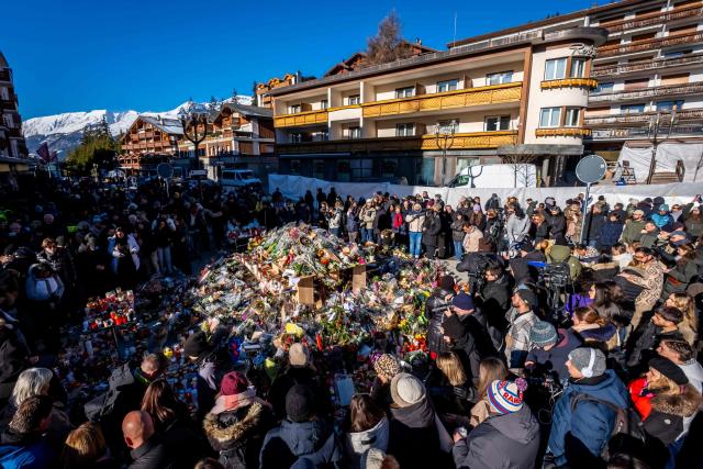 People gather around a makeshift memorial to pay their respects by laying flowers, candles and messages near the Constellation bar, on January 4, 2026, in Crans-Montana in honour of the victims of the fire that ripped through the venue in the luxury Alpine ski resort on New Year's Eve. Authorities investigating the New Year's blaze in the Swiss resort of Crans-Montana have identified 24 of the 40 people killed, including 11 minors and six foreign nationals, police said on January 4, 2026. Also 119 were injured during the fire, most of them seriously, according to the latest toll. (Photo by MAXIME SCHMID / AFP)